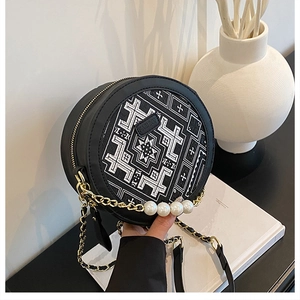 Detail view of round leather crossbody bag with geometric embroidery and pearl chain