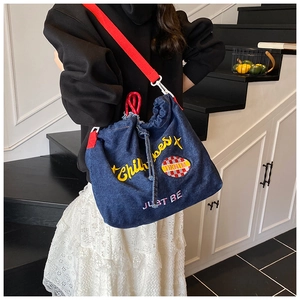 Detail of navy denim crossbody bag with Childhood embroidery and red webbed strap
