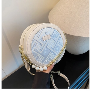 Close-up of circular crossbody bag with blue floral embroidery and pearl chain strap