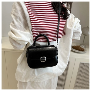 Detail of black glossy square handbag with silver metal buckle and adjustable strap
