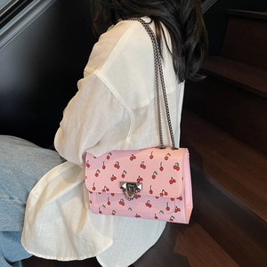 Sac bandoulière rose à motif cerise avec chaîne en métal porté par un mannequin