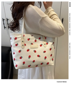 Détail du sac cabas à imprimé fraises avec plaque logo jaune sur fond en toile blanche