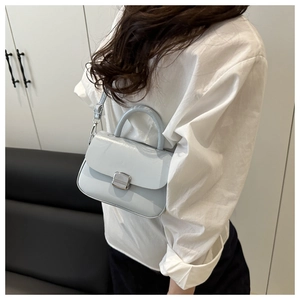 Detail of light blue square crossbody bag with silver lock worn by a model in lifestyle setting