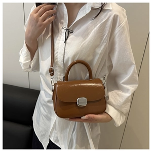 Detailed shot of brown glossy leather crossbody bag with silver buckle on a model