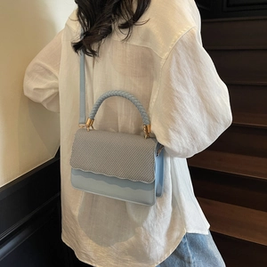 Sac à main bleu clair avec rabat tissé et bordure en cuir ondulé porté par un modèle