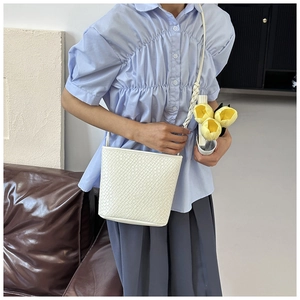 Close-up of white bucket bag featuring woven strap and crocodile embossed leather texture
