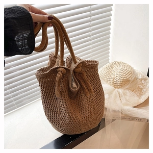 Vue détaillée du sac cabas marron tissé avec des pompons décoratifs et une poignée à nœud