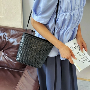 Chic black woven bucket bag with shoulder strap shown on model in a stylish indoor setting