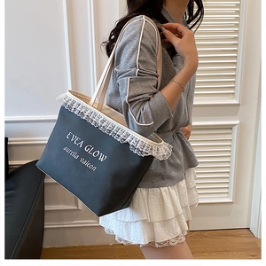 Detailed close-up of a black canvas tote bag featuring delicate white lace trim and text