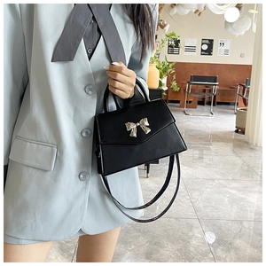 Detail of elegant black crossbody bag with silver bow accent and top handle style