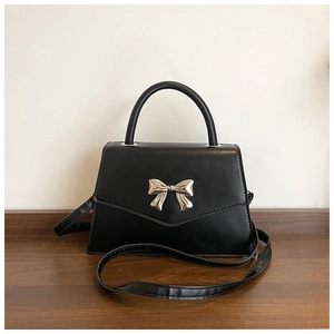 Detail of silver bow metal buckle on elegant black trapezoid handbag with PU leather texture