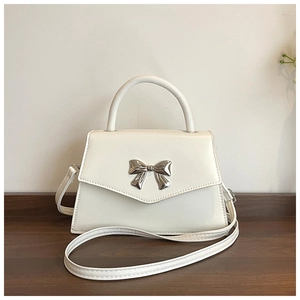 Detail of white leather crossbody bag featuring a decorative silver metal bow clasp