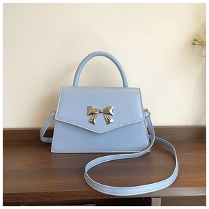 Detailed close-up of light blue trapezoid handbag with gold bow clasp on wooden stand