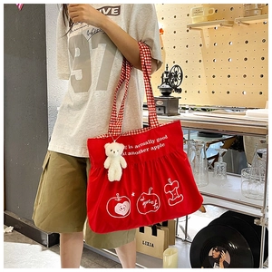 Detail of red canvas tote bag with apple print, checkered handles and cute bear charm