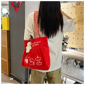 Detail of red travel tote bag featuring apple print, checkered strap and bear charm