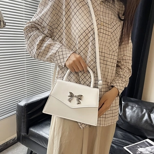 White faux leather crossbody bag with a metallic silver bow on the front flap