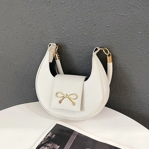 Detailed close-up of white semi-moon bag with golden bow clasp and leather texture