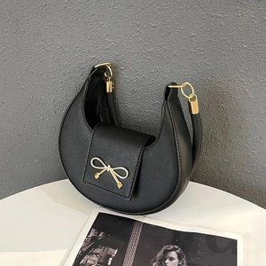 Detailed macro view of black Saffiano leather texture and golden bow buckle on the bag