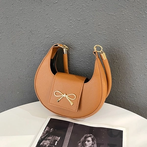 Detail of cross-grain leather finish and golden bow buckle on brown crescent bag