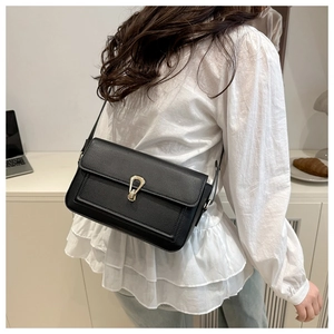 Détail d'un sac bandoulière en cuir noir grainé avec une boucle dorée en fer à cheval