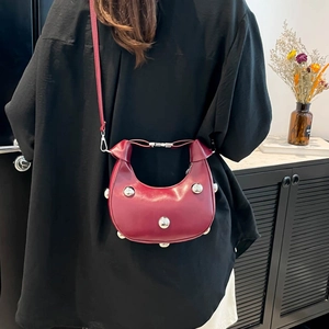 Deep red matte leather half-moon shoulder bag with silver studs on a model