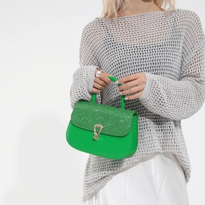 Sac à main vert avec rabat scintillant et boucle dorée sur fond blanc impeccable