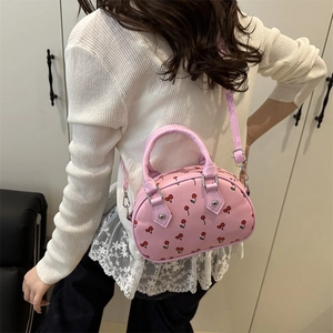 Sac à main rose à motif cerise en cuir PU avec bandoulière, porté par un mannequin chic