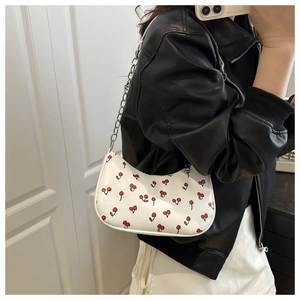 Close-up of white cherry print shoulder bag with silver chain worn by a model