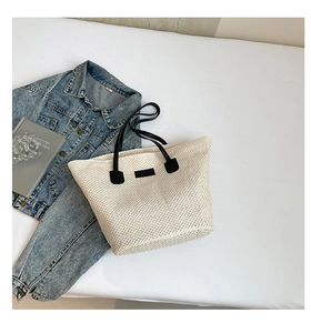 Top-down view of cream woven straw bucket bag with black straps and denim jacket