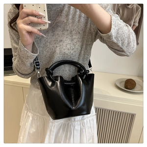 Detail of black glossy leather cloud bag showing woven handles and crossbody strap