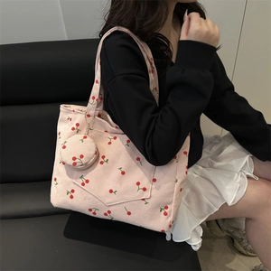 Pink corduroy tote bag with cherry patterns and small coin purse on a leather bench