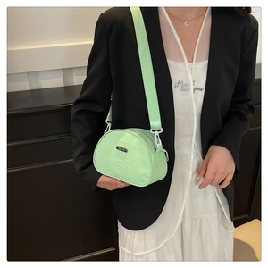 Detail of mint green nylon shell bag with metal logo and wide woven shoulder strap