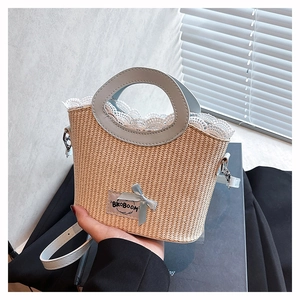 Détail d'un sac seau en paille avec bordure en dentelle blanche et nœud papillon bleu