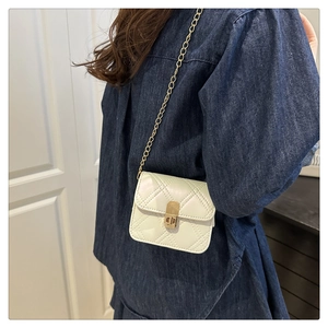 Detail of a mini quilted crossbody bag with gold chain and twist lock on a denim outfit