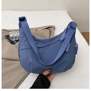Detail of blue nylon crescent bag with wide strap and woven zipper pull shown in hand