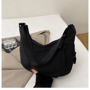 Detail view of black nylon dumpling bag featuring adjustable wide strap and woven zipper puller