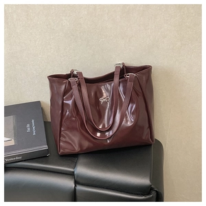 Détail du sac cabas bordeaux avec nœud en métal argenté sur un banc en cuir