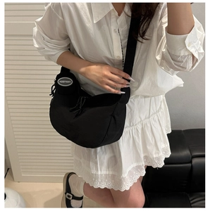 Détail d'un sac bandoulière noir en forme de lune porté avec une chemise blanche et jupe
