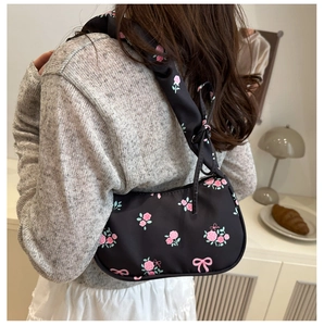 Détail d'un sac d'épaule noir avec motifs de roses roses et sangle à volants