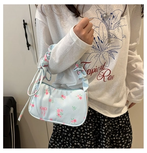 Détail du sac baguette bleu clair avec motifs roses, nœuds et poignée à volants