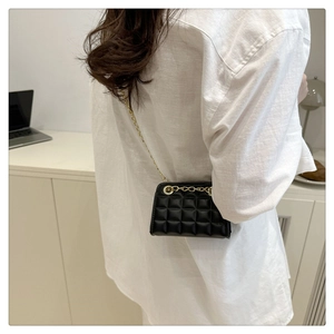Détail d'un mini sac carré noir matelassé avec chaîne dorée porté par un mannequin