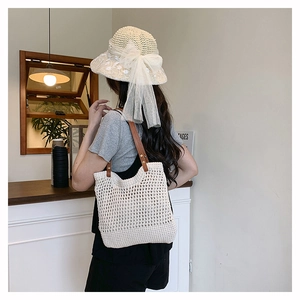 Dettaglio borsa in maglia crema con manici in pelle e cappello in paglia ricamato