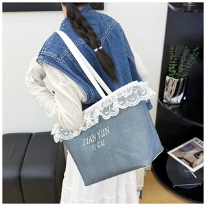 Détail du sac cabas en denim bleu avec bordure en dentelle blanche et lettrage brodé