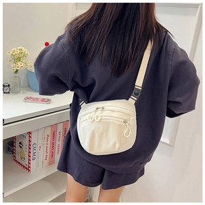 Detail view of a beige nylon crossbody chest bag featuring multiple zipper pockets