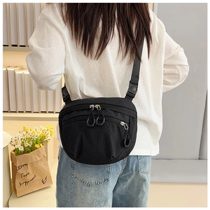 Detail of black nylon crossbody bag with double zippers on model in a cozy setting