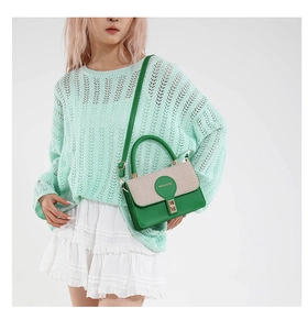 Detail of green leather handbag with beige woven flap and gold metal buckle on model