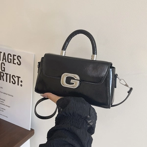 Detail of glossy black leather crossbody bag with sparkling rhinestone G metal buckle