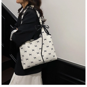 Detail view of the large black bow tie on a white canvas shoulder bag for women