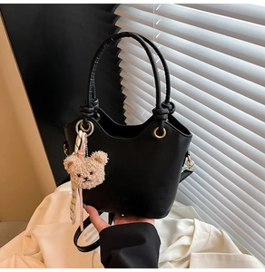 Détail du sac seau noir mat avec poignée ronde dorée et accessoire d'ourson marron