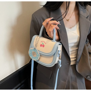 Detail view of stylish light blue saddle bag featuring cherry print and donut charm